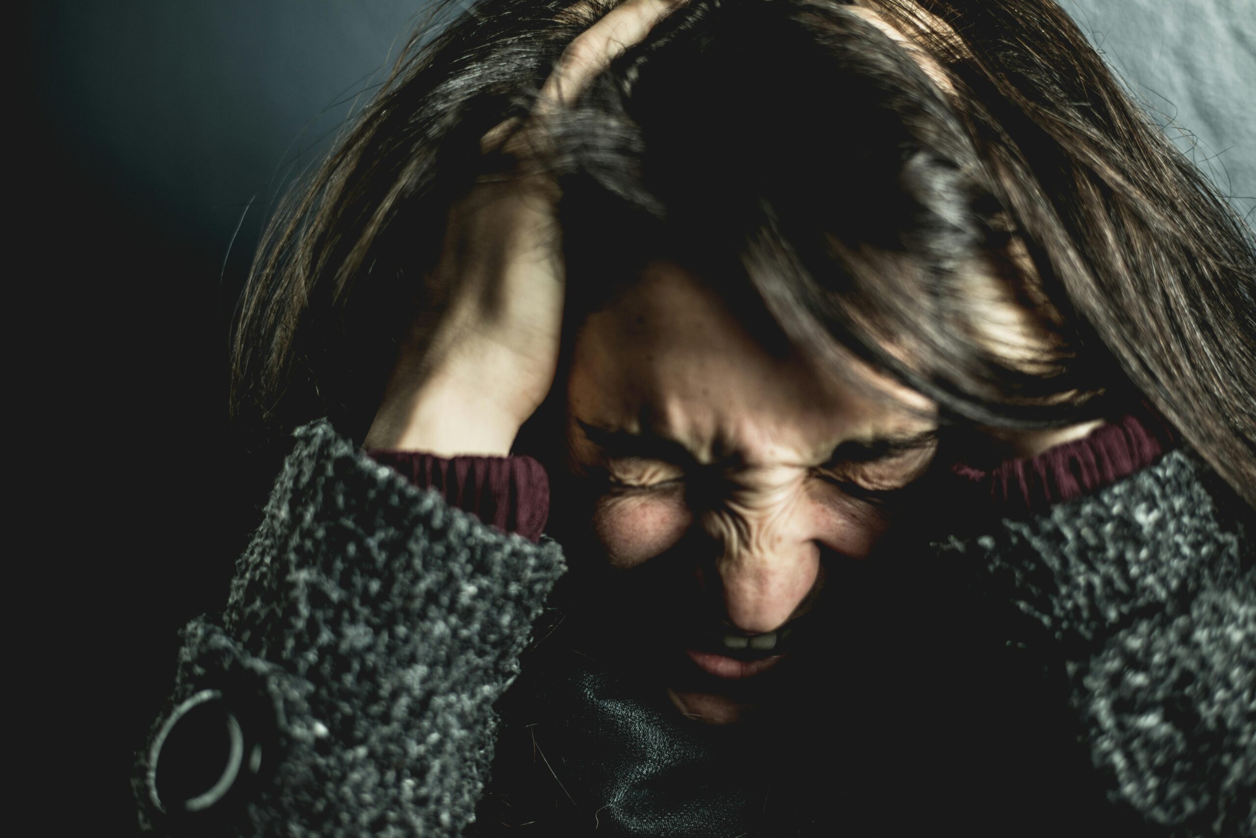 Young woman sitting alone with head in hands, showing signs of emotional stress and deep pain
