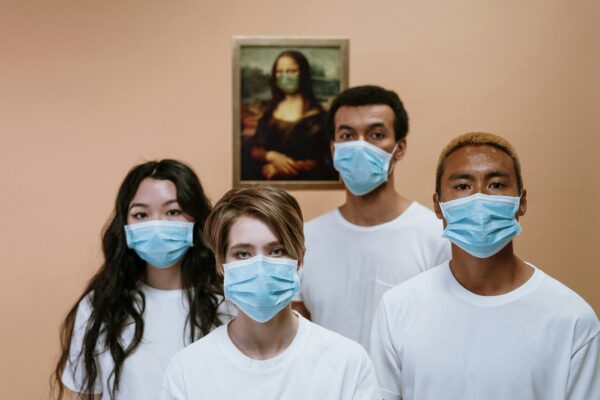 A diverse group wearing masks stands in front of a masked Mona Lisa painting.