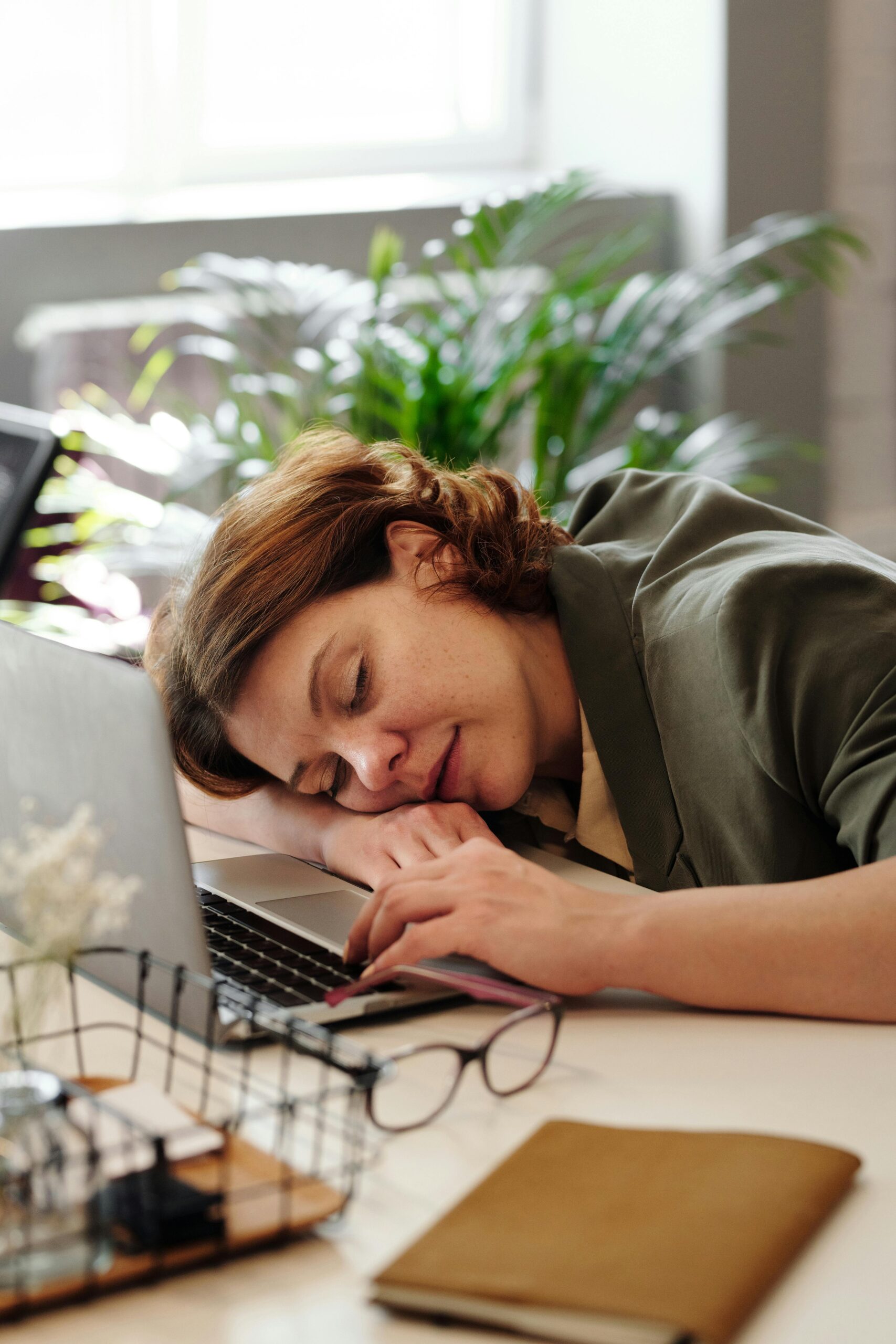 Tired woman in home office resting on laptop, illustrating burnout.