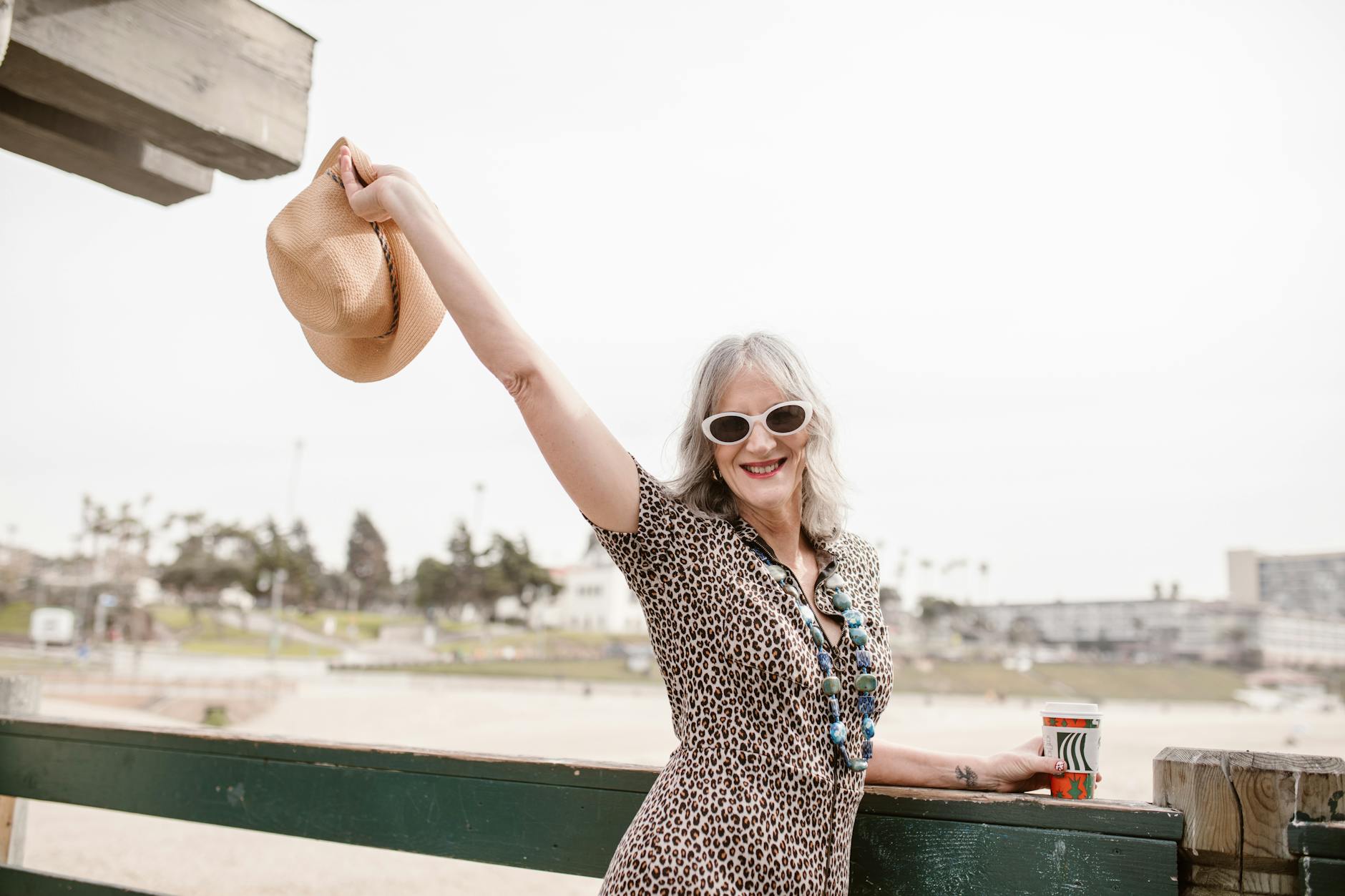 Stylish senior woman with hat at the beach, embracing life joyfully.