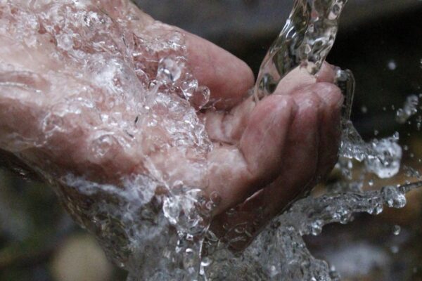 Close-up of a human hand under a stream of clear, flowing water.